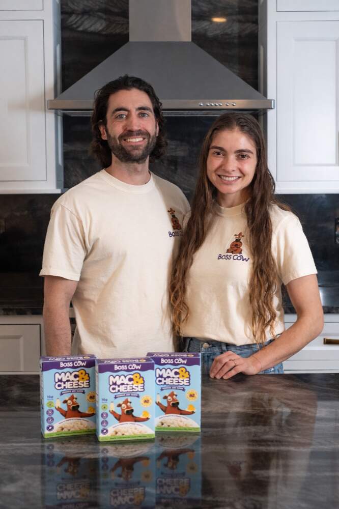 Boss Cow co-founders Kevin and Samantha Dwoskin in branded tees with three boxes of A2 mac & cheese