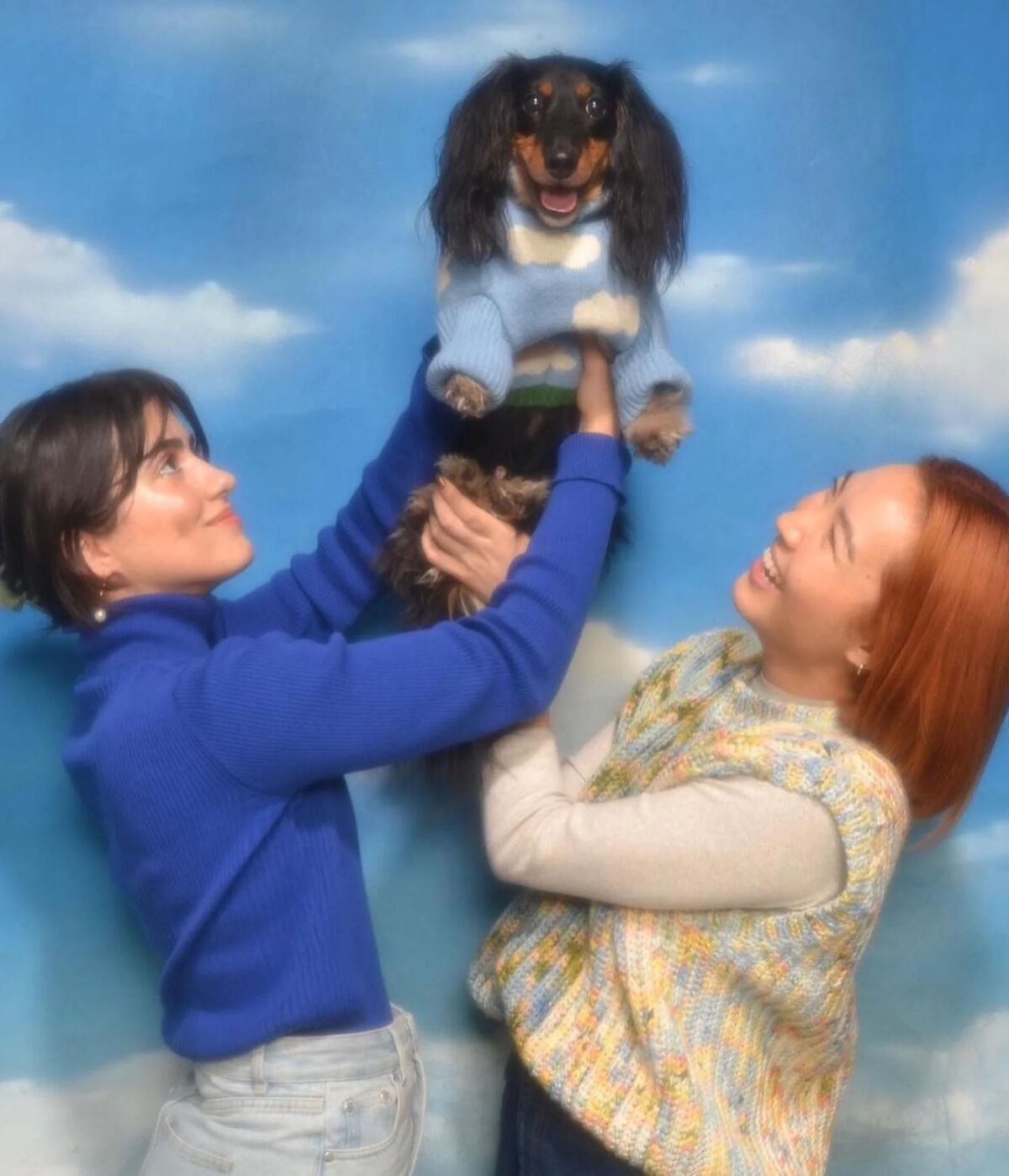 Little Beast founders Jisu Kim (left) and creative director Lys Bui (right) lifting a dachshund in a knit sweater